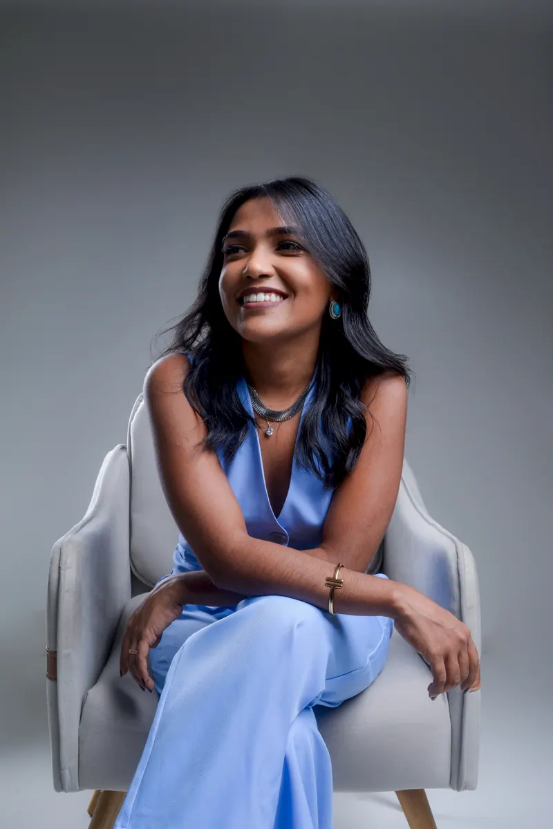 Samara Farias sorrindo, de macacão azul-claro, sentada numa poltrona cinza